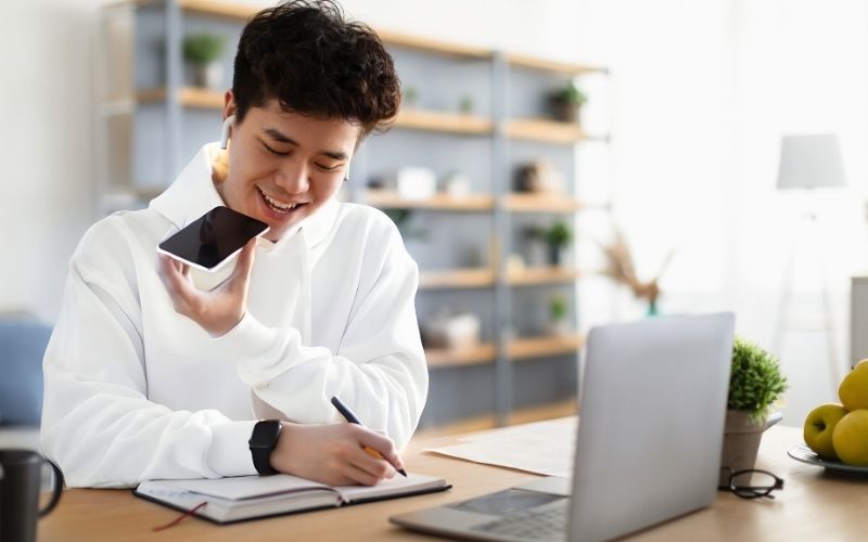 Smiling virtual assistant working from home while taking notes during a phone call with a client.